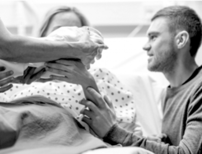 A midwife hands a newborn to her parents. 