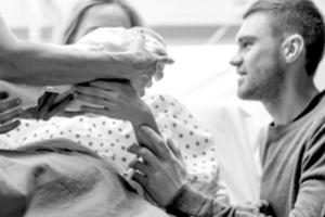 A midwife hands a newborn to her parents. 