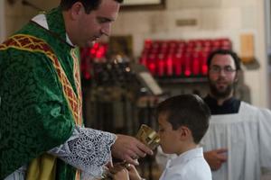 Above, Bishop Steven Lopes provides the Precious Blood at first Communion for St. Alban’s Catholic Church, an ordinariate parish in Rochester, N.Y. Below, children receive first Communion at St. Joseph Oratory in Detroit.