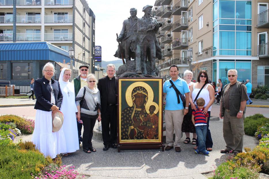 The icon of Our Lady of Czestochowa, also known as the Black Madonna, in front of the statue of Lewis and Clark, with the Pacific beach in the background. Father West stands with the icon.