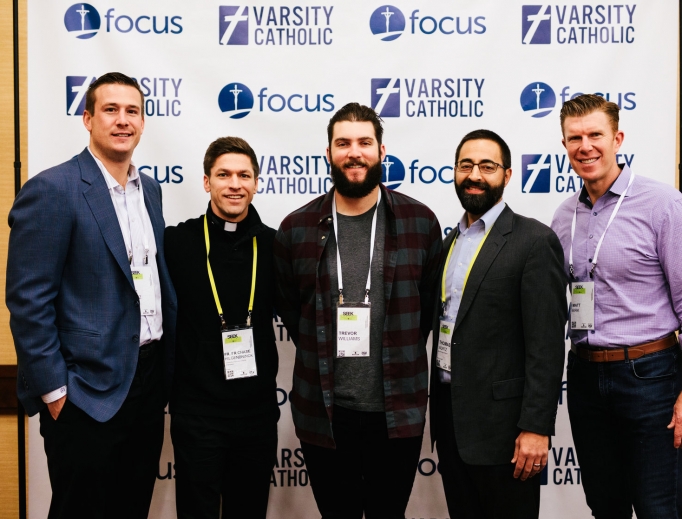 Above, l to r:Joe Reitz (former NFL player), Father Chase Hilgenbrinck (former MLS player), Trevor Williams (starting pitcher for the Pittsburgh Pirates), Thomas Wurtz of Varsity Catholic and Matt Birk (former NFL player) attend a Varsity Catholic event at the 'Seek' conference hosted by Fellowship of Catholic University Students. Below, Wurtz (l) and Lou Holtz (c) chat with Calvin Mueller (r) at 'Seek.'