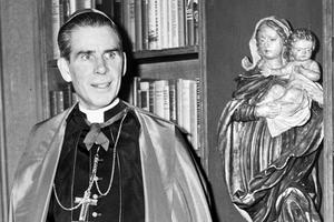 Bishop Fulton Sheen stands before a bookcase on the set of his Dumont television program.