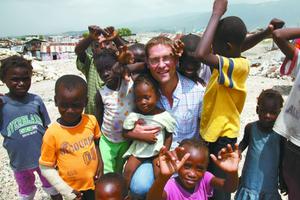 Mary’s Meals assists children from Haiti (shown above with founder Magnus MacFarlane) and across the globe. Below, MacFarlane greets children eating a meal provided by Mary’s Meals in Malawi. 