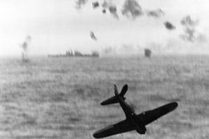 A Japanese Zero Kamikaze crashes into the sea after trying to hit the aircraft carrier USS Essex (CV-9) off Okinawa, May 14, 1945. The vessel in the background is a U.S. Navy Cleveland-class light cruiser.
