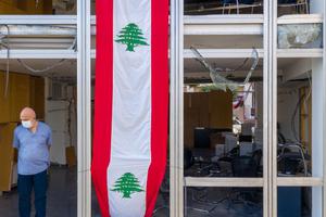 A man stands in the window of a damaged high-rise building, draped with banner in the style of the Lebanese flag, on August 12, 2020 in Beirut, Lebanon. The explosion at Beirut's port last week killed over 200 people, injured thousands, and upended countless lives. There has been little visible support from government agencies to help residents clear debris and help the displaced, although scores of volunteers from around Lebanon have descended on the city to help clean. 