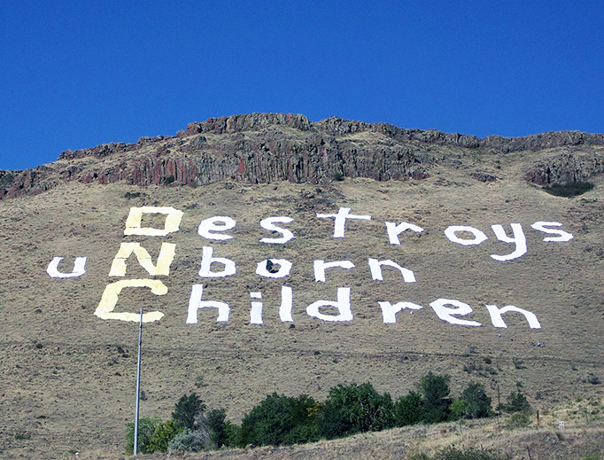 Abortion protest sign on North Table Mountain outside Denver, during the 2008 Democratic National Convention. The sign reads "(DNC) Destroys uNborn Children" and is made of sheets sown together.