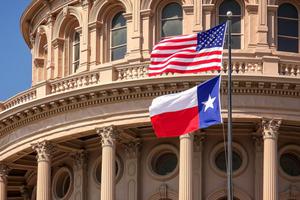American and Texas state flags flying on the dome of the Texas State Capitol building in Austin.