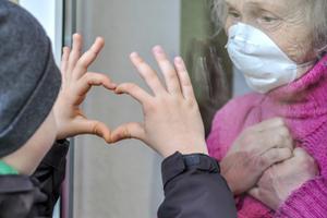 A grandmother in a respiratory mask communicates with her grandchild through a window amid the coronavirus pandemic. 