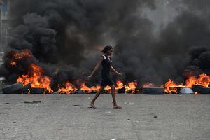 A woman walks past tire barricades set ablaze by demonstrators protesting in Port-au-Prince against Haitian President Jovenel Moise Feb. 10. 