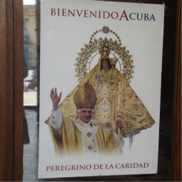 Pope Benedict will celebrate an outdoor Mass in Santiago de Cuba this afternoon. A poster in Cuba refers to him as a 'pilgrim of charity.'