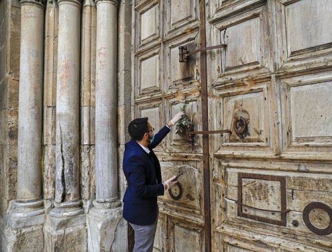 A worshipper hangs an olive branch on the closed door of Holy Sepulcher Church during Palm Sunday in Jerusalem's Old City, amid movement restrictions due to the COVID-19 coronavirus pandemic, on April 5.