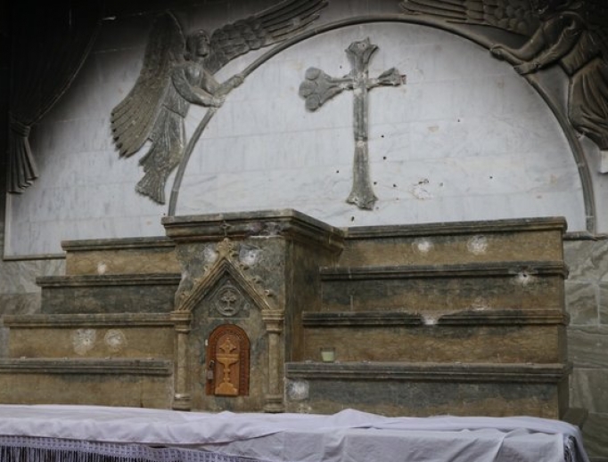 Signs of the unspeakable violence perpetrated on Iraqi Christians by the Islamic State: Above, bullet holes and a defaced cross mar the main altar of St. Addai’s Church in Karemlash. Below,
Chaldean Father Thabet Yousif pokes through the rubble that was once his family home; a torn red curtain marks what is left of the sanctuary of St. Mary the Virgin Church in Karemlash; the tomb of martyred priest Father Ragheed Ganni; and Ghazala, an Iraqi Christian who resisted Islamic State militants when they overthrew her town.