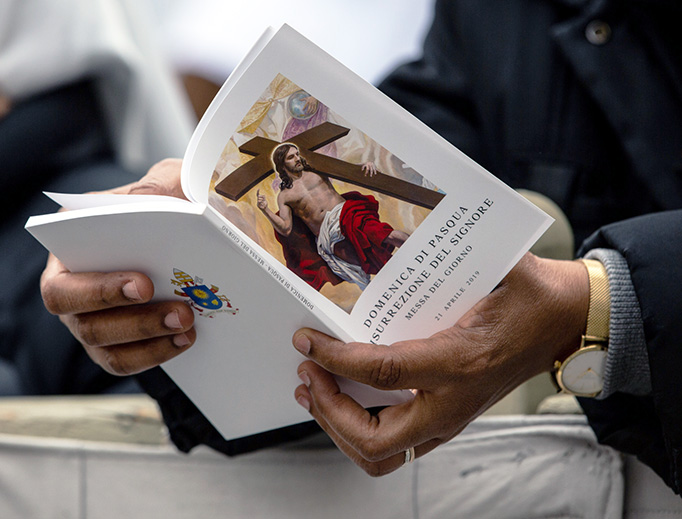 A pilgrim follows along with a booklet as Pope Francis celebrates Easter Mass and the Urbi et Orbi Blessing in St. Peter's Square, April 22, 2019.