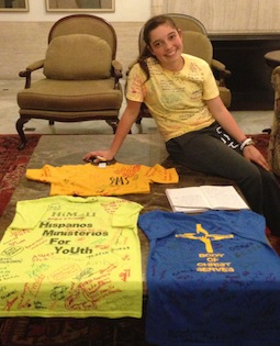 Alina Ramos poses with the four shirts she used to raise money for her trip to WYD 2013. In front of her is a daily journal she uses to document her experiences in Rio