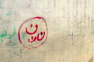 ISIS militants marked Christian houses and property in Mosul by painting the symbol ن, signifying that they were to be seized after their ultimatum in 2014. ن is the Arabic letter for “N” and is the first letter of the Arabic word for Christian, “Nasrani.” The letter ن became a global symbol of support of the Iraqi Christians. The Christians displaced by ISIS painted the symbol themselves on the side of the bathrooms in one of the refugee camps in Erbil. 