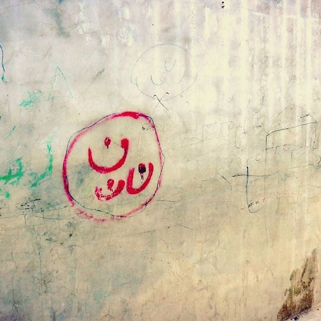 ISIS militants marked Christian houses and property in Mosul by painting the symbol ن, signifying that they were to be seized after their ultimatum in 2014. ن is the Arabic letter for “N” and is the first letter of the Arabic word for Christian, “Nasrani.” The letter ن became a global symbol of support of the Iraqi Christians. The Christians displaced by ISIS painted the symbol themselves on the side of the bathrooms in one of the refugee camps in Erbil. 