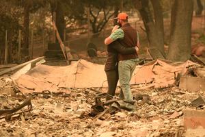 Above, Chris and Nancy Brown embrace Nov. 12 while looking over the remains of their burned residence after the Camp Fire tore through the region in Paradise, California. Below, Alameda County Sheriff Coroner officers search for human remains at a burned residence in Paradise on Nov. 12, and a welcome sign remains near a burned residence in Paradise.