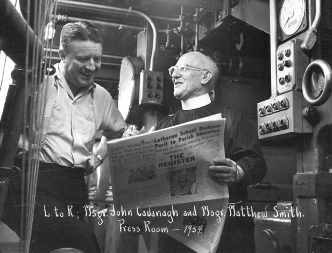 Msgr. Matthew Smith discusses a new issue of the National Catholic Register with Msgr. John Cavanaugh in the press room in Denver. 
