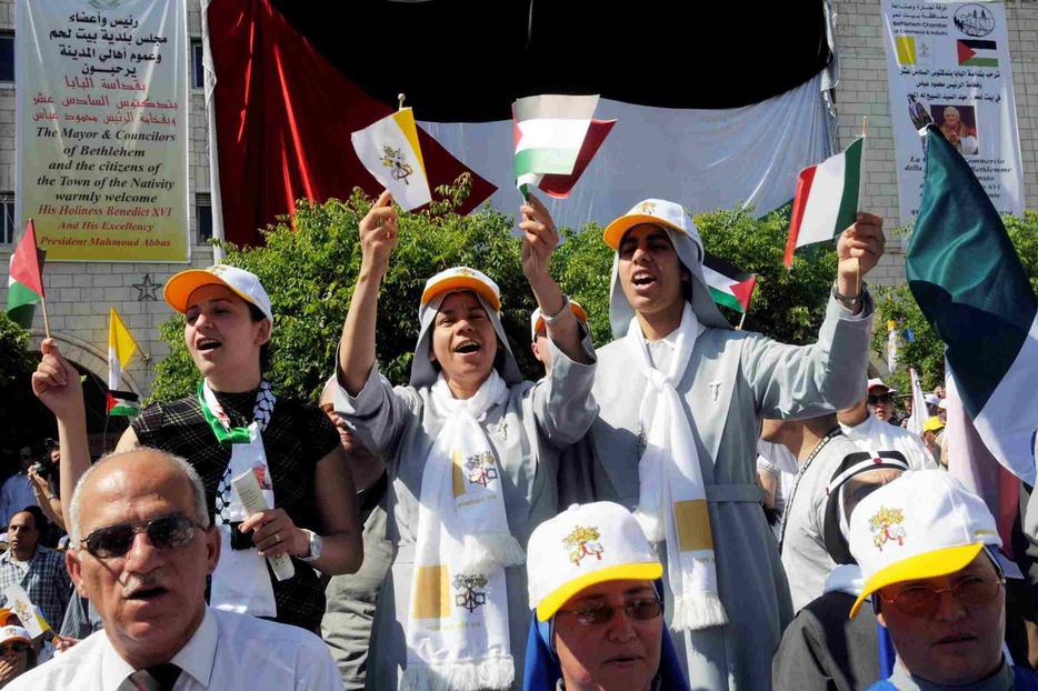Nuns sing while holding Vatican and Palestinian flags as Benedict celebrates Mass in Manger Square in Bethlehem.