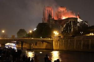 People stand on the banks of the River Seine as flames engulf the Notre-Dame Cathedral in Paris on April 15, 2019.
