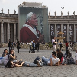 A giant image of Pope John Paul II is seen as youth from Barcelona, Spain, relax in St. Peter's Square at the Vatican April 29. They were among pilgrims arriving for the May 1 beatification of Pope John Paul II.