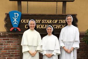 From l to r: Sister Mariana, Sister Daniela and Sister Maria Caeli pose in front of the school sign. 