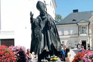 Above, a statue of John Paul II in a Wadowice square. Below, the Wadowice basilica (exterior and interior showing portrait and relics), the John Paul II Family Home Museum and the yellow house where the saint lived in Krakow. Other photos showcase displays at the Wadowice museum, including his skis and rings that John Paul II gave to Benedict XVI and a photo of the papal pair.