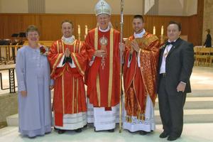Father Justin (next to his mother) and Father Joshua Waltz (next to his father), shown with their parents, Herb and Theresa. Bishop Paul Zipfel presided at the Cathedral of the Holy Spirit in Bismarck, North Dakota. Below, framed manutergia in the Waltz home: one is behind, showing around the edges. Also shown: Father Jordan Dosch at his first Mass, June 1, at Cathedral of the Holy Spirit, presents the special cloth to his mother, Lynne Dosch. He had just explained the custom before presenting it to his mother. His father, Vernon, is to the left of Lynne.
