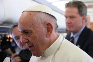 Pope Francis, with Vatican spokesman Greg Burke in the background, speaking to journalists aboard the papal plane to Sweden.
