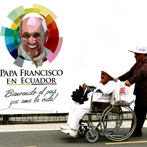  A woman is wheeled past a banner with an image of Pope Francis at Samanes Park, where Pope Francis celebrated Mass in Guayaquil, Ecuador.