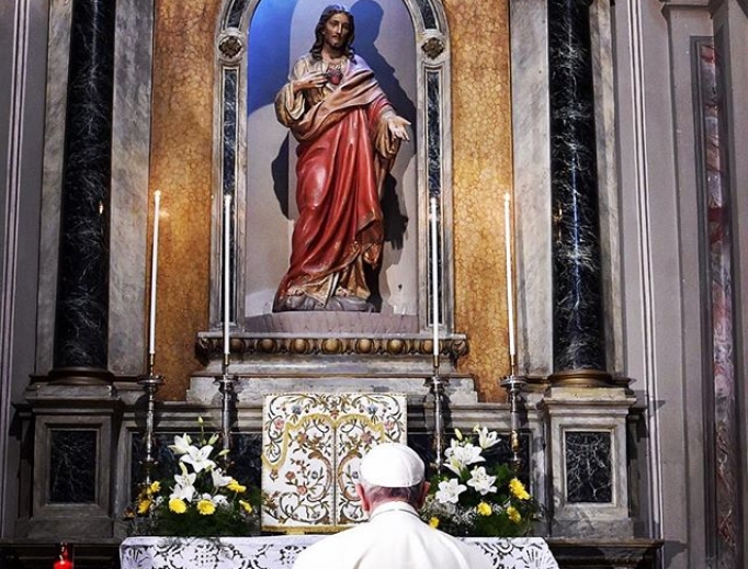 Pope Francis prays before Sacred Heart of Jesus statue.