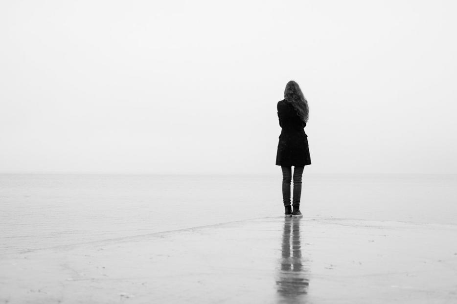 A woman stands alone against a bleak horizon.