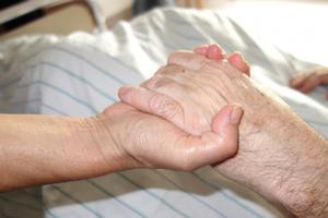 A daughter holds her mother's hand in the hospital.