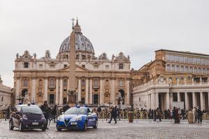 A crowd of people and police cars in  front of St. Peter's Square.