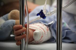 A child clasps metal bars of hospital bed.