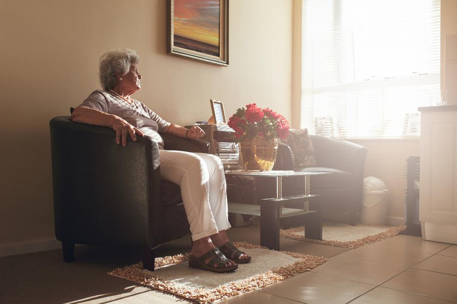 An elderly woman sits alone in her room.