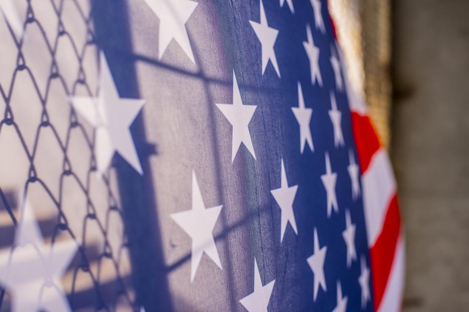 An American flag is shown draped over a border fence.