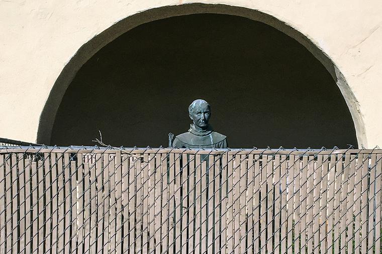 A bronze statue of St. Junípero Serra, located at the entrance to the Old Mission Santa Inés, is surrounded by a chain link fence to protect it on Nov. 2, 2020, in Solvang, California.