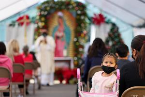 A girl wears a face covering as Father Rafael Saiz holds Christmas Mass outdoors at St. Mary's Catholic Church on Dec. 25, 2020, in Los Angeles.