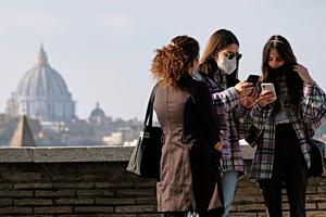 Women wearing protective masks look at their smartphone on a terrace of the Orange Garden (Giardino degli Aranci) on the Aventine Hill overlooking St. Peter's Basilica in Rome on Nov. 11, 2020.