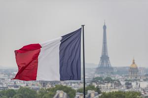 French flag waves above Paris with the Eiffel Tower in the background.