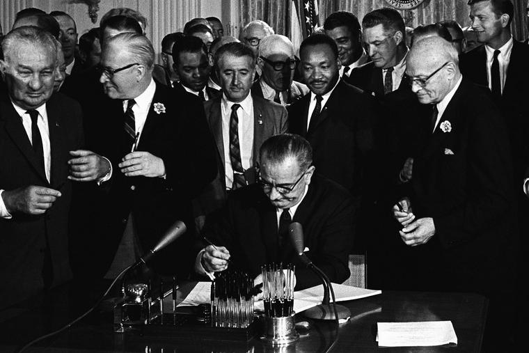 With Dr. Martin Luther King, Jr., looking on, President Lyndon B. Johnson signs into law the Civil Rights Act on July 2, 1964.