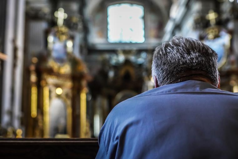 A man sits alone inside a Catholic church praying.