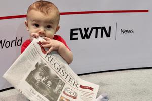 A young baby consuming every page of the National Catholic Register newspaper.
