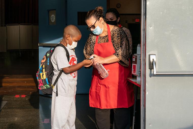 A Catholic school employee helps a student sanitize before entering the classroom in the Archdiocese of New York at Immaculate Conception School.