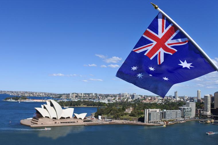 The National flag of Australia flies above the Sydney Harbor and the Opera house in Australia.