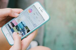 A woman holds a smartphone with the Instagram app displayed.