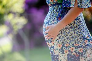 A pregnant woman stands alone in the park.