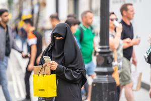 A woman wearing a niqab, using mobile phone while shopping.