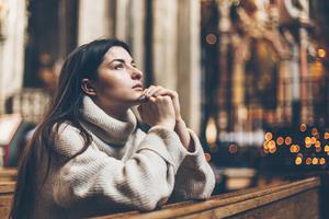 A young female parishioners sits praying at a Catholic church.